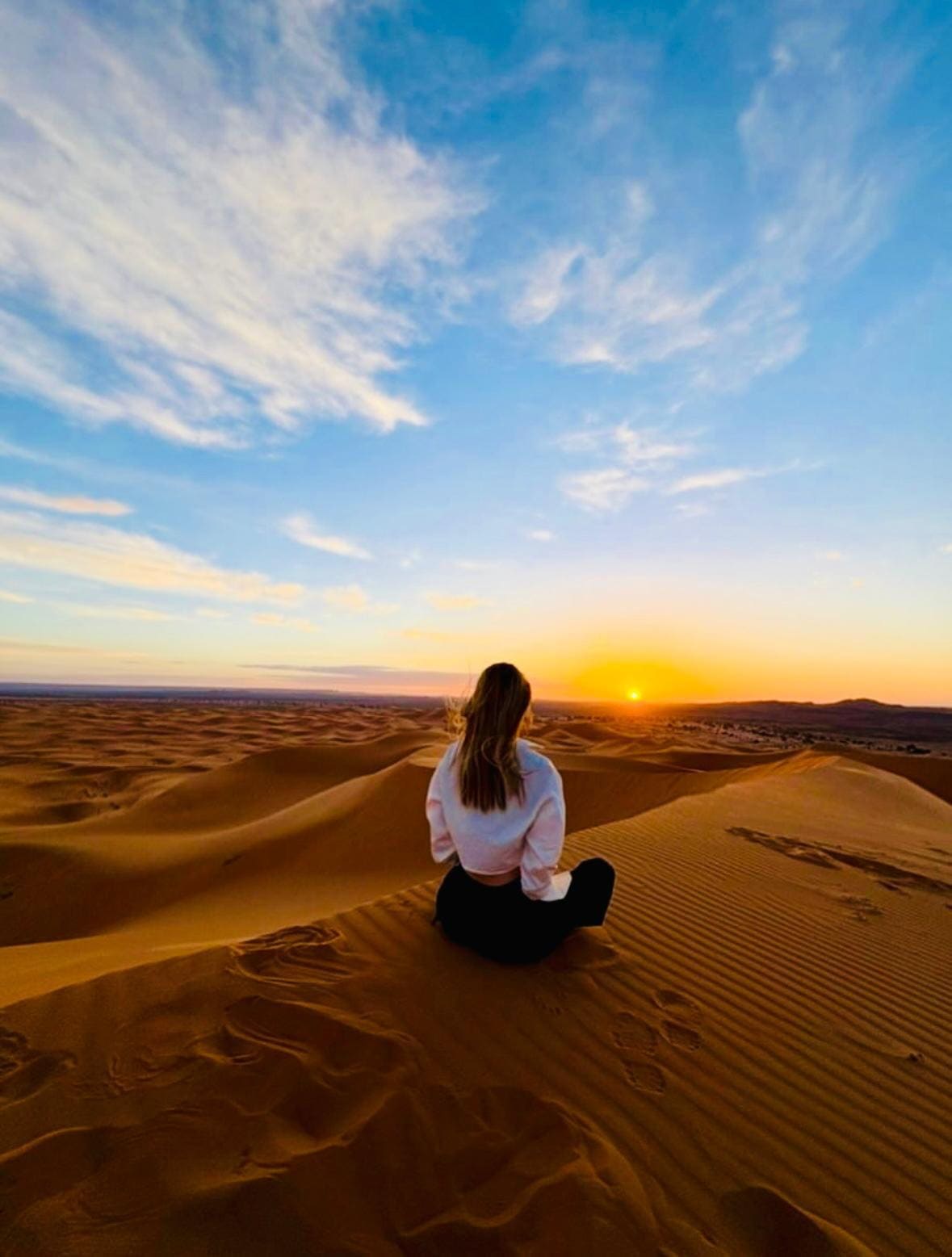 Viajera contemplando el amanecer sentada en lo alto de una duna